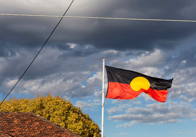 Aboriginal flag flying high above community centre in suburban neighbourhood.